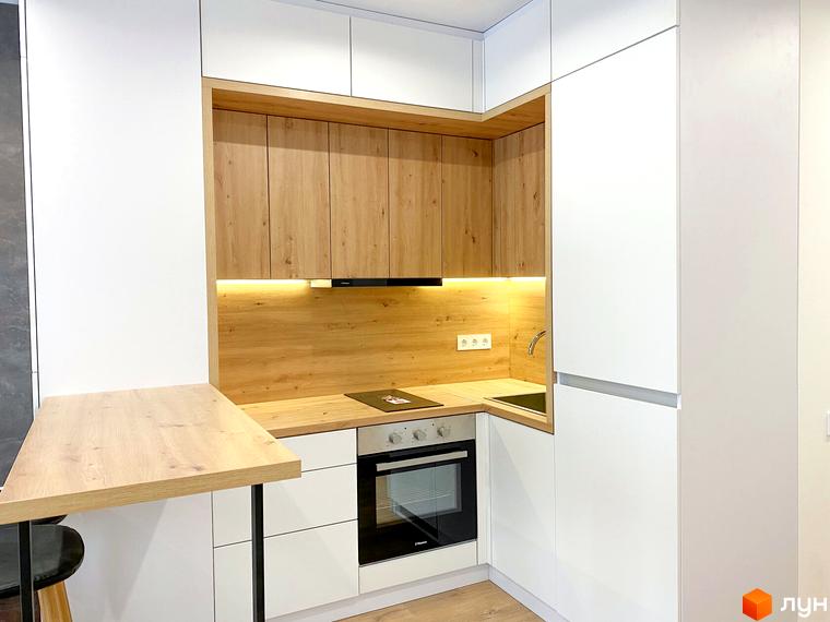 Інтер'єр кухні в житловому комплексі Coliving EST: білі шафи, дерев'яні стільниця та фартух, вбудована техніка та барна стійка.