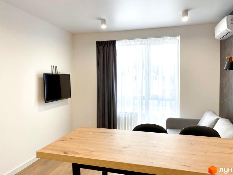 Світлий інтер'єр квартири в Coliving EST з обідньою зоною та вітальнею. Кімната облаштована телевізором та має велике вікно.