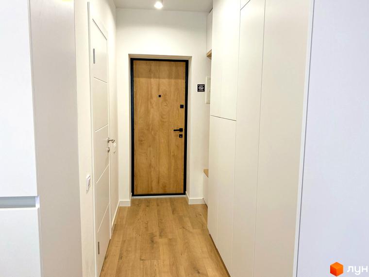 Передпокій з дерев'яними дверима та білими шафами в житловому комплексі Coliving EST. Стильний дизайн інтер'єру з дерев'яною підлогою.