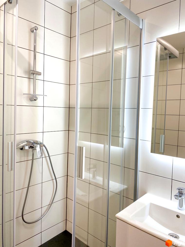 Ванна кімната в Coliving EST: душова кабіна зі скляними дверима, біла плитка, раковина та дзеркало з підсвічуванням.