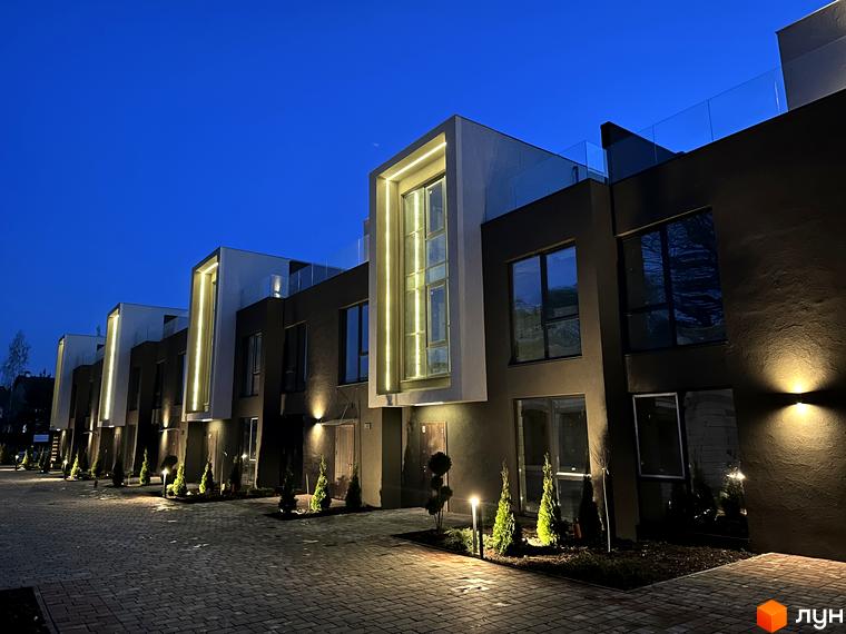 Будинок Elwood Townhouse з підсвіткою фасаду та скляним балконом. Навколо будинку викладена бруківка та висаджені туї.