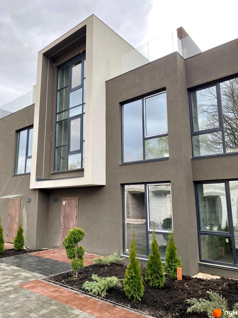 Зовнішній вигляд Elwood Townhouse з великими вікнами та сірим фасадом, поруч доглянутий двір з туями та бруківкою.
