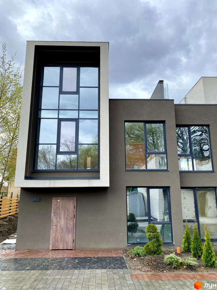 Будинок Elwood Townhouse з великими вікнами та сірим фасадом. Поруч розташовані зелені насадження та вимощена доріжка.