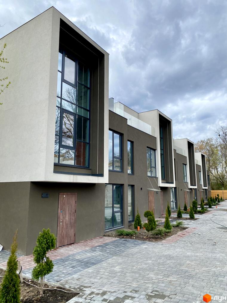 Зовнішній вигляд Elwood Townhouse з великими вікнами та сірим фасадом, впорядкована прибудинкова територія з бруківкою та туями.