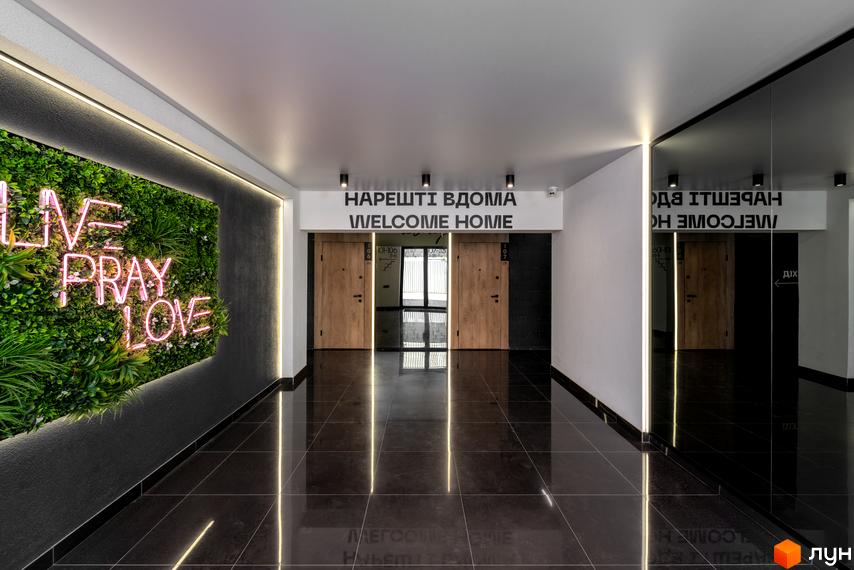 Інтер'єр вестибюля житлового комплексу Coliving Akadem з глянцевою підлогою, декоративною зеленою стіною та написом 