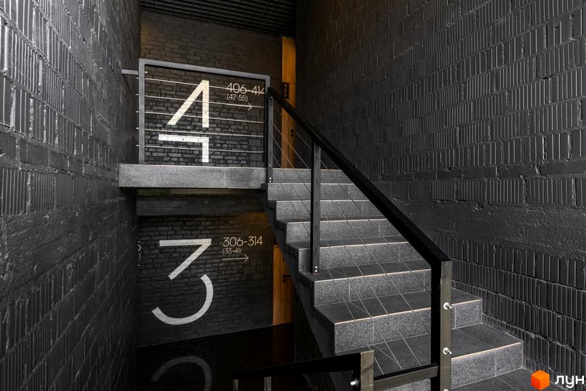 Сучасний дизайн сходової клітини в житловому комплексі Coliving Akadem з великими цифрами поверхів та вказівниками.