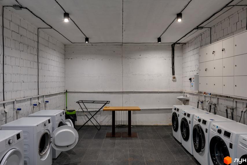 Пральня житлового комплексу Coliving Akadem з рядами пральних машин, сушаркою та шафками для зберігання.