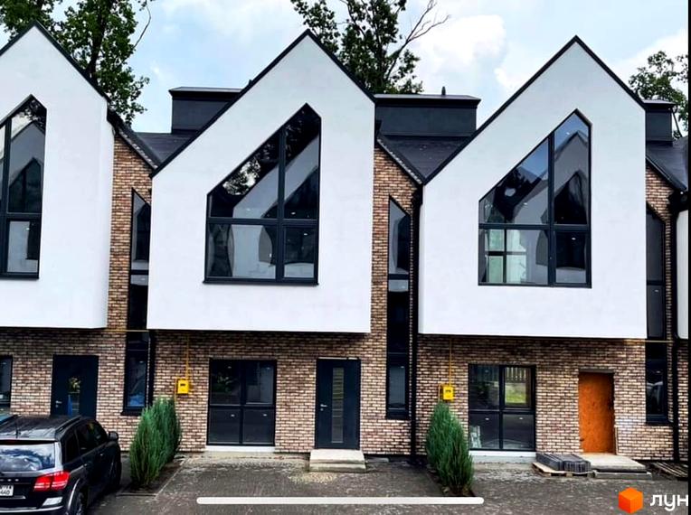 Зовнішній вигляд таунхаусів Dream Town 2 з цегляними фасадами та великими вікнами. Перед будинками розташована прибудинкова територія з деревами та автомобілем.