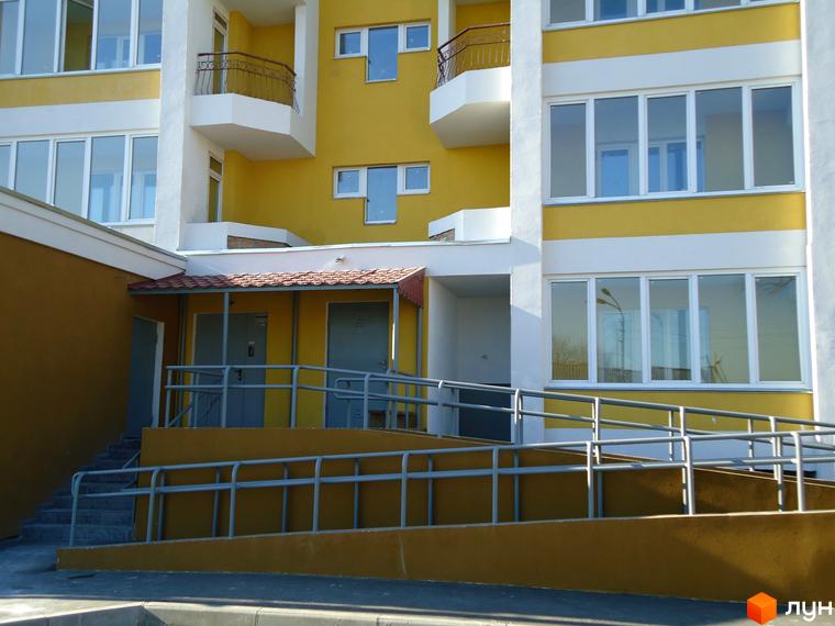 Зовнішній вигляд новобудови ЖК Гостомельський квартал з жовтими фасадами та великими вікнами. Біля будинку розташований пандус та сходи.