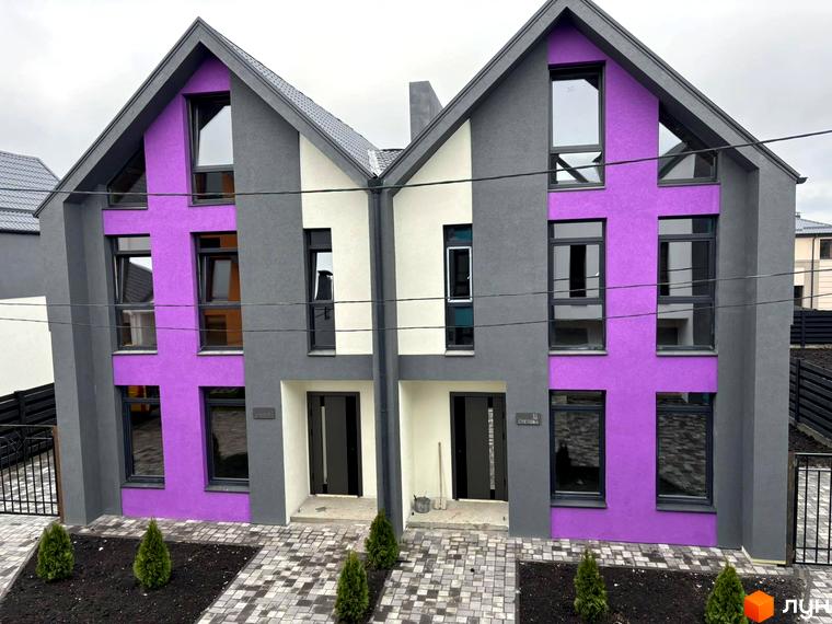 Фасад двоповерхового будинку з великими вікнами та фіолетовою стіною. Перед будинком викладена бруківка та висаджені туї.