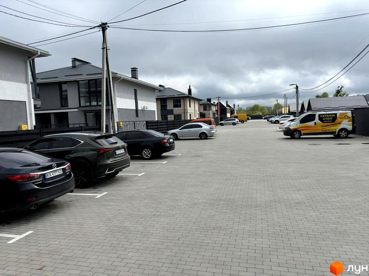 Зображення житлового комплексу КМ Beverly Hills Residence з парковкою та будинками з сірими фасадами. На території видно автомобілі та асфальтовані доріжки.