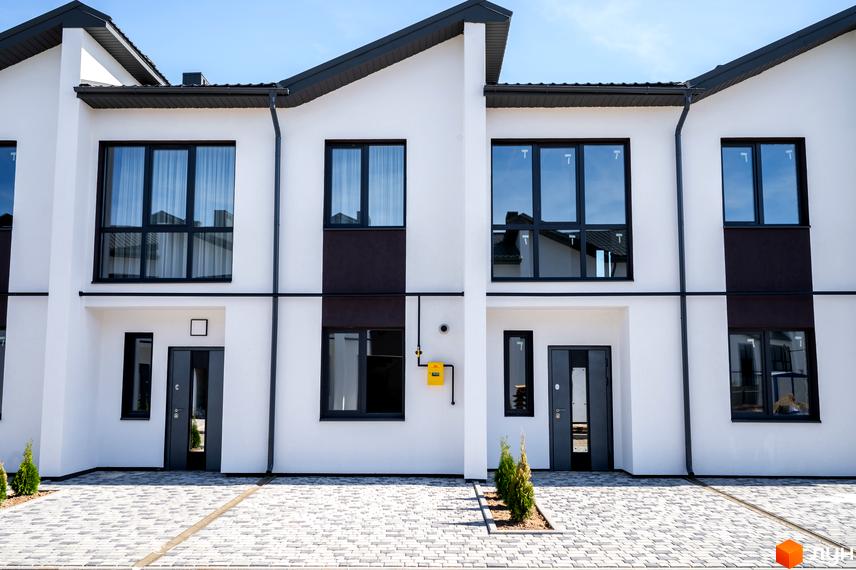 Білі таунхауси Котеджного містечка WEST TOWN з темними дахами та вікнами. Перед будинками вимощена бруківка та невеликі зелені насадження.