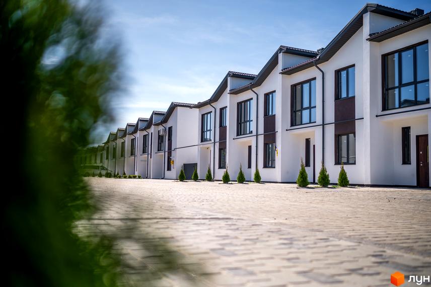 Зовнішній вигляд таунхаусів WEST TOWN з білими фасадами та темними вікнами. На передньому плані вимощена бруківкою дорога.