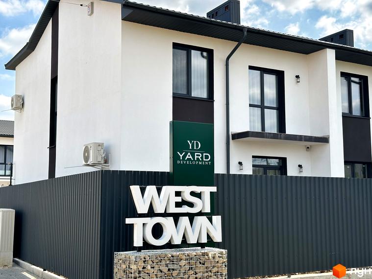 Зображення таунхаусів WEST TOWN з білими фасадами та чорними вікнами. Перед будинками розташований темний паркан та об'ємні літери WEST TOWN.