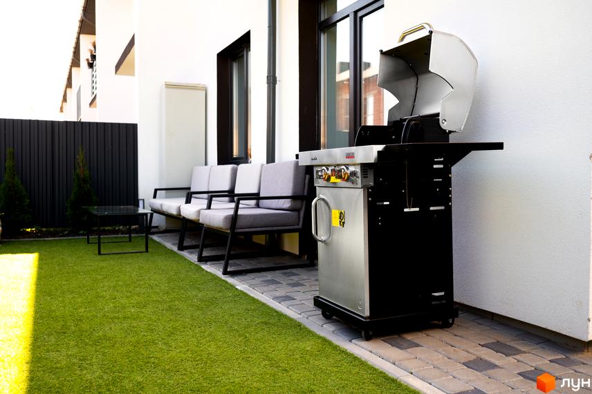 Зображення таунхаусів WEST TOWN з газовим грилем на подвір'ї. На задньому плані видно місця для відпочинку та зелений газон.