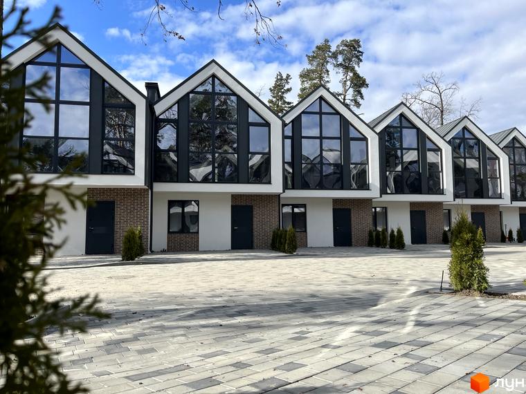 Фасад таунхаусів Lucky Town з великими вікнами та темними дверима. Бруківка на прибудинковій території, зелені насадження.