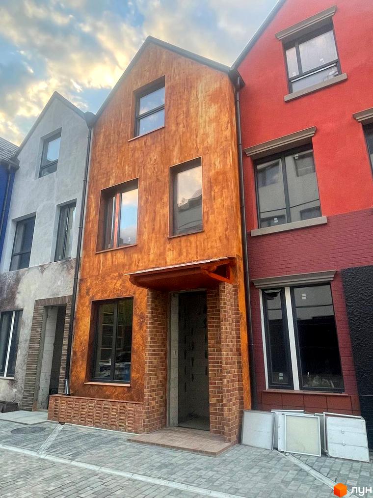 Фасад будинку житлового комплексу КМ КАDЕНЮК homes з цегляною кладкою та декоративною штукатуркою, вимощена бруківкою прибудинкова територія.