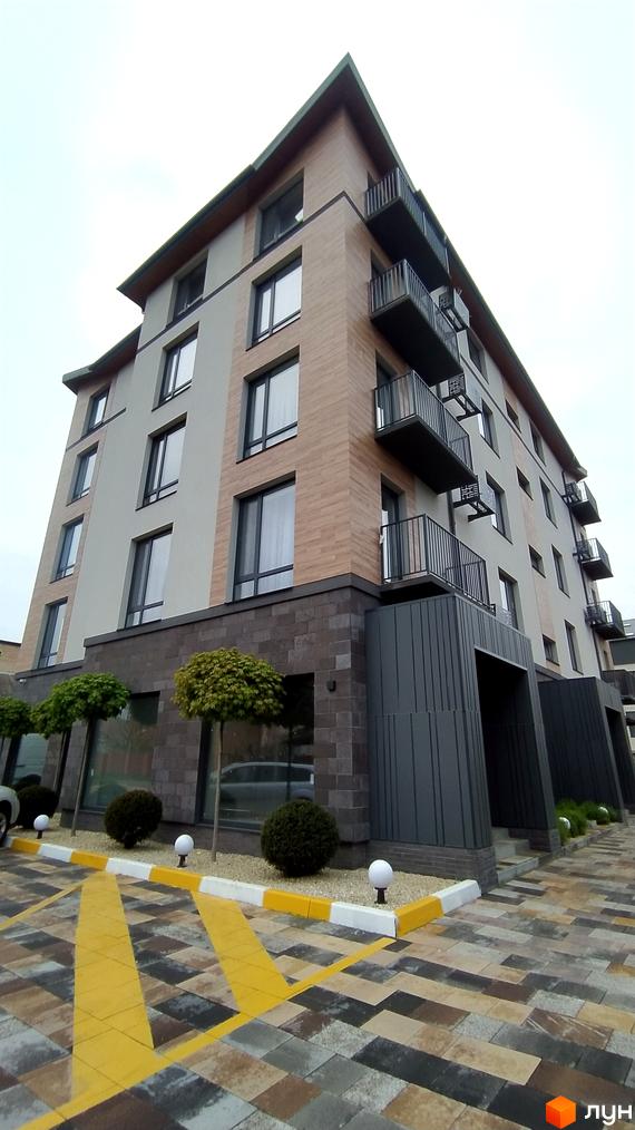 Зовнішній вигляд новобудови пров. Урожайний, 16 з балконами та вікнами, прибудинкова територія з бруківкою та деревами.