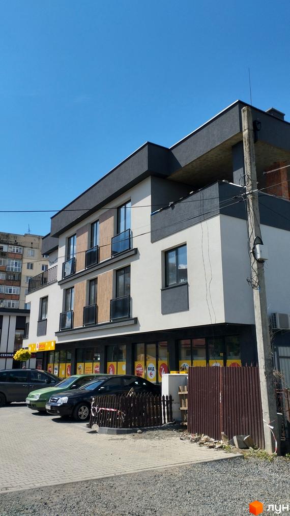 Фасад житлового комплексу на вулиці Олексія Бестужева-Рюміна, 7, з паркуванням та зеленими насадженнями. Будинок має кілька поверхів, сучасні вікна та балкони.