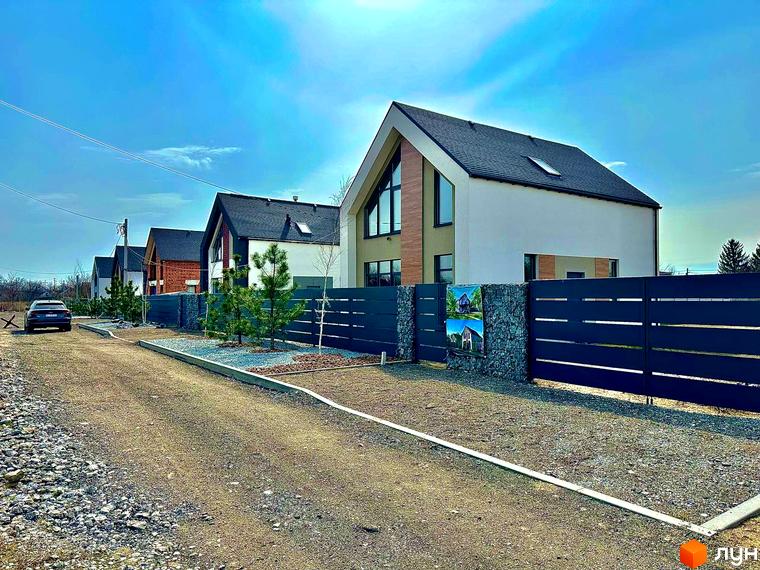 Котеджне містечко КМ Fill House. Сучасні будинки з темним дахом та великими вікнами, розташовані вздовж дороги з гравійним покриттям та зеленими насадженнями.