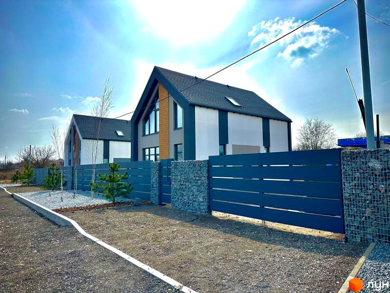 Котеджне містечко КМ Fill House: два будинки з темним дахом та білими стінами, огороджені парканом з металевих ламелей та кам'яними стовпами. Прибудинкова територія з гравієм та молодими соснами.