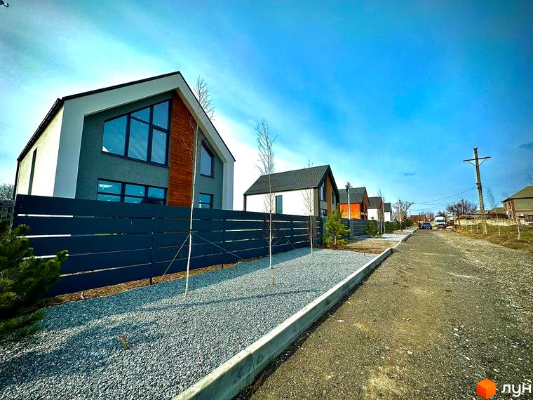 Сучасний котеджне містечко КМ Fill House з сірими фасадами та великими вікнами, огороджений темним парканом. Прибудинкова територія засипана гравієм, з молодими деревами.