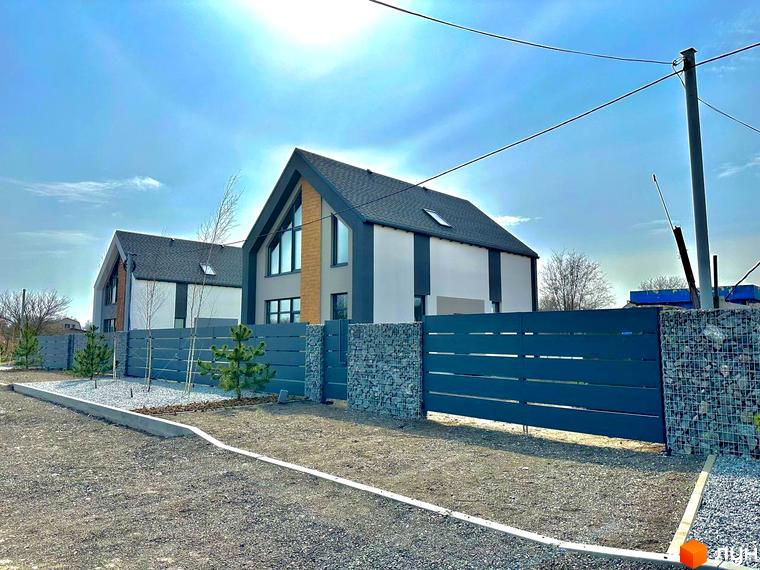 Котеджне містечко Fill House: двоповерхові будинки з сірою покрівлею та великими вікнами, огороджені парканом з габіонними стовпами. Прибудинкова територія з гравієм та молодими деревами.