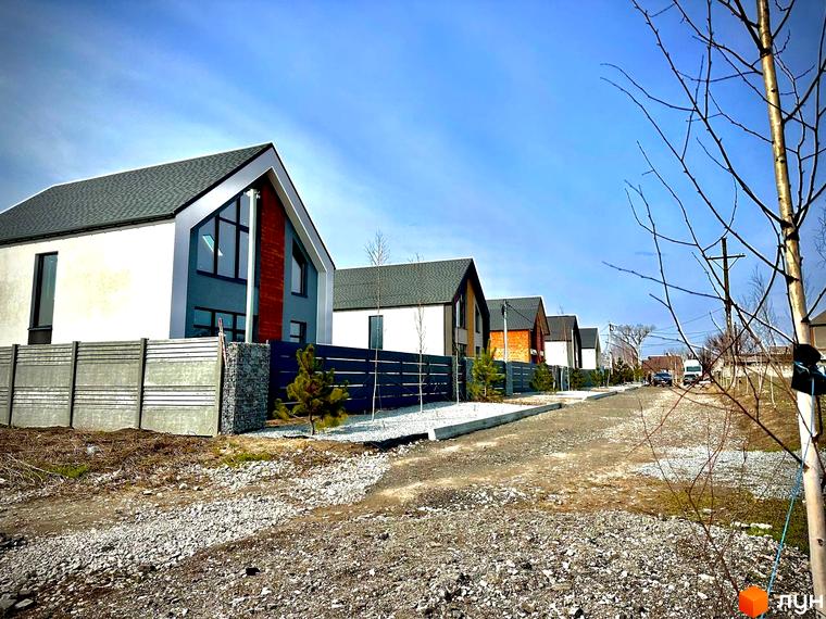 Котеджне містечко КМ Fill House: фасади будинків з панорамними вікнами та сірими дахами, огороджена територія з бруківкою та молодими деревами.