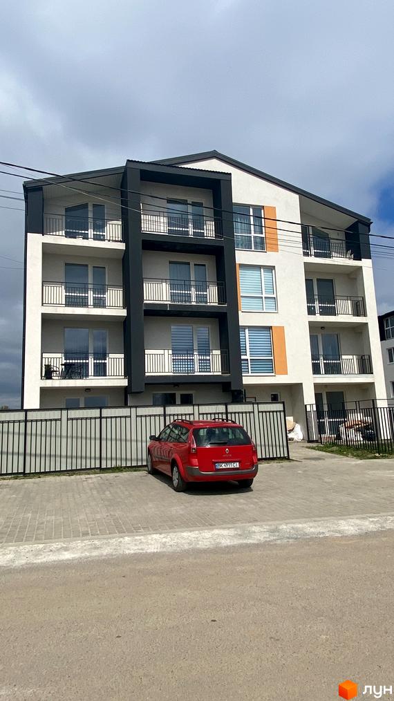 Зовнішній вигляд житлового комплексу Club House з балконами та вікнами, прибудинкова територія з червоним автомобілем та парканом.