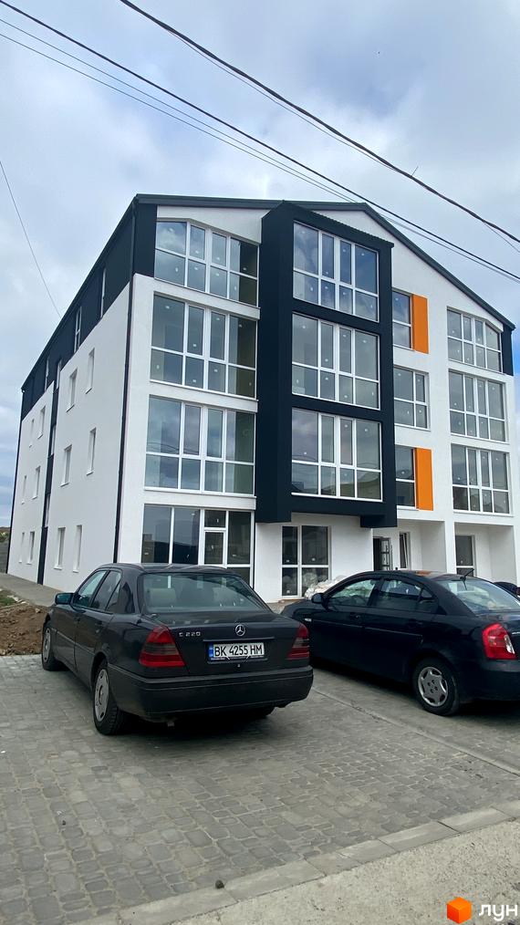 Зовнішній вигляд новобудови ЖК Club House з великими вікнами та чорними елементами фасаду, прибудинкова територія з бруківкою та автомобілями.