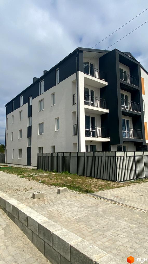 Зовнішній вигляд житлового комплексу Club House з біло-чорним фасадом та балконами. Прибудинкова територія з огорожею та вимощеною плиткою.