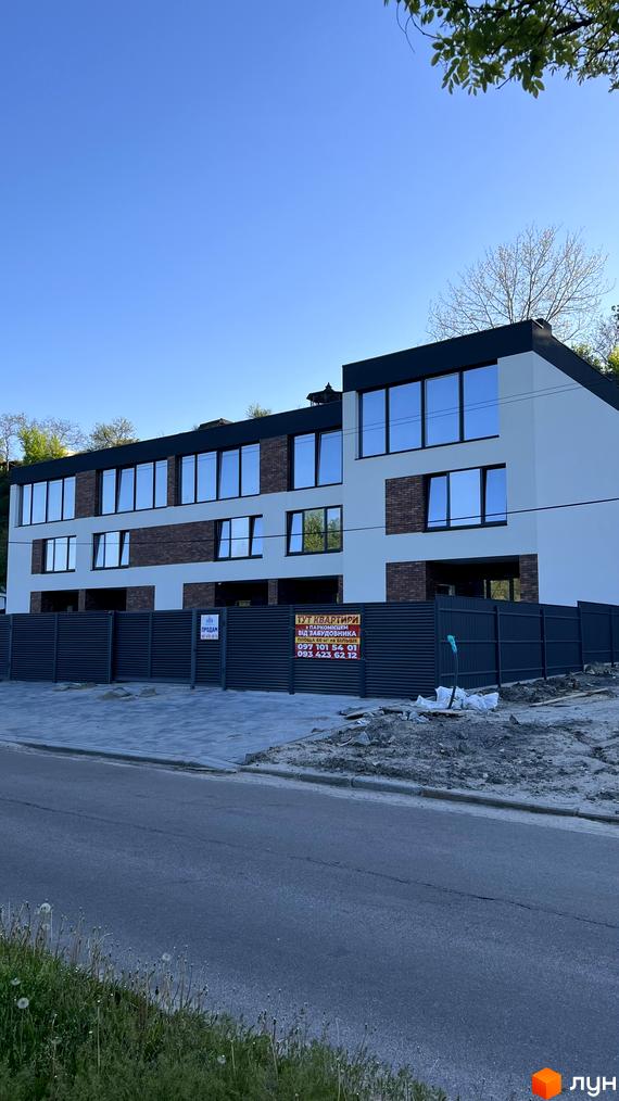 Будинок з цегляним та білим фасадом, великими вікнами та сірим парканом. На території новобудови облаштований двір та дорога.