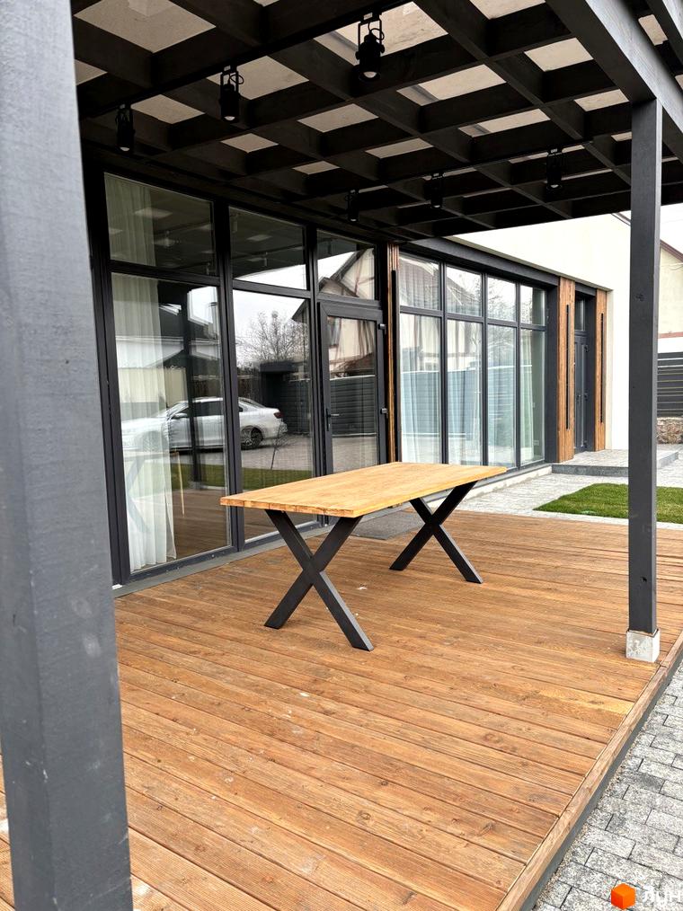 Зовнішній вигляд будинку КМ Romankiv House з терасою та дерев'яним столом. Прибудинкова територія з газоном та бруківкою.