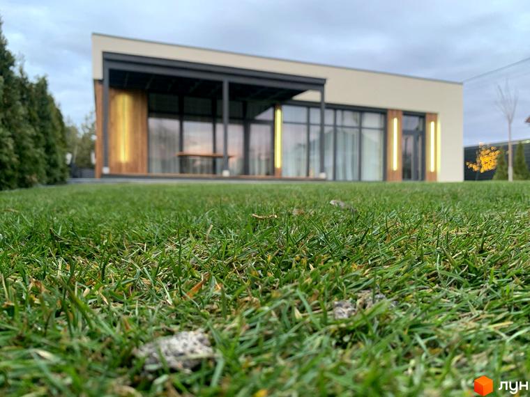 Котеджне містечко Romankiv House з великими вікнами та зеленою галявиною перед будинком. Зовнішній вигляд будинку з підсвічуванням та прибудинкова територія.