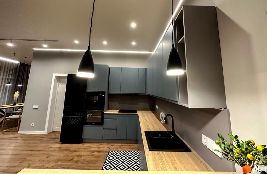 Сучасна кухня з сірими шафами, дерев'яною стільницею та чорним змішувачем. На підлозі килим з геометричним візерунком.