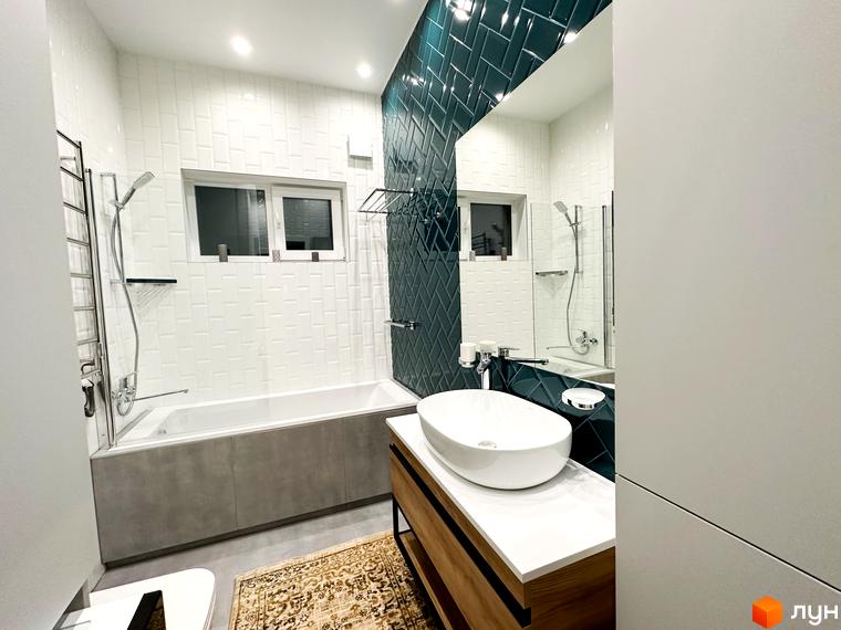 Сучасна ванна кімната з білою плиткою та бірюзовою плиткою на стіні, білою ванною та раковиною, дерев'яною тумбою. КМ Romankiv House – ваш дім біля природи.