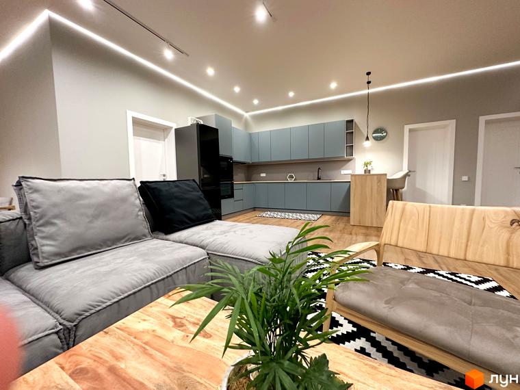 Інтер'єр вітальні з кухнею в світлих тонах, великий диван та сучасна кухня. КМ Romankiv House – ваш новий дім.