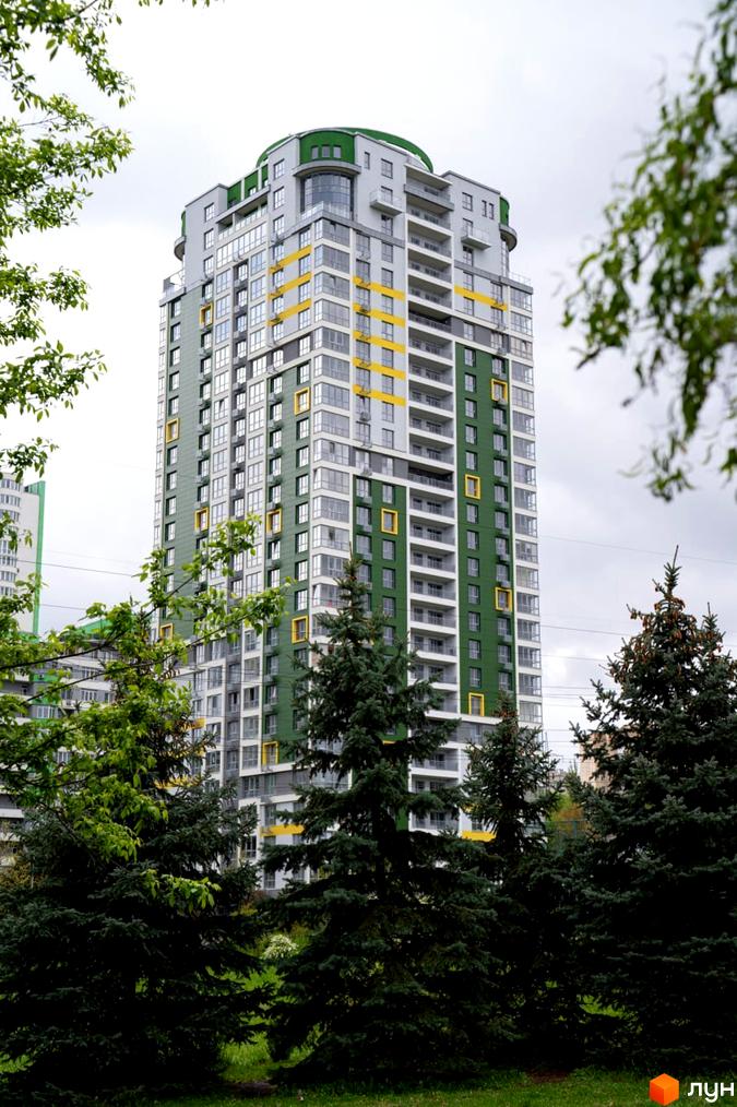 Багатоповерховий житловий будинок Житлового комплексу Паркове місто з фасадом зеленого, сірого та жовтого кольорів, оточений зеленими деревами та доглянутим газоном.