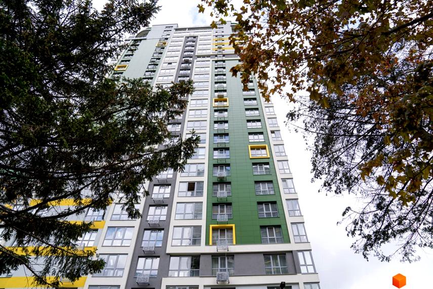 Житловий комплекс Паркове місто: багатоповерхова новобудова з зеленим, сірим та білим фасадом, деякі вікна мають жовті рами. Навколо будинку видно дерева.