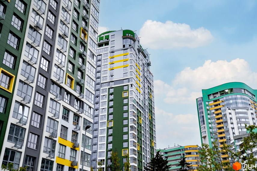 Житловий комплекс Паркове місто: високі будинки з фасадами темно-зеленого, сірого та білого кольорів, доповнені жовтими акцентами. Навколо будівель видно дерева.