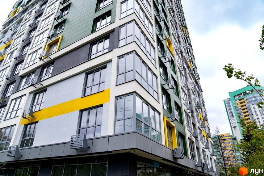 Багатоповерховий будинок Житлового комплексу Паркове місто з фасадом сірого, білого, темно-зеленого кольорів та жовтими акцентами. Поруч зелені насадження.