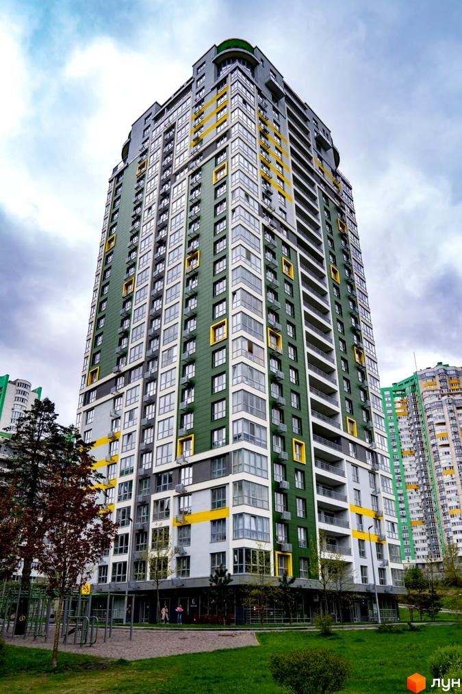 Багатоповерховий будинок Житловий комплекс Паркове місто з темно-зеленим та жовтим фасадом. Навколо будинку зелені газони та дитячий майданчик.