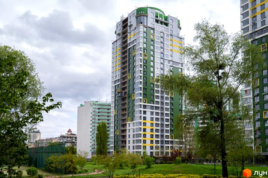 Житловий комплекс Паркове місто: висотний будинок з зелено-жовтим фасадом серед паркової зони з деревами та газонами.