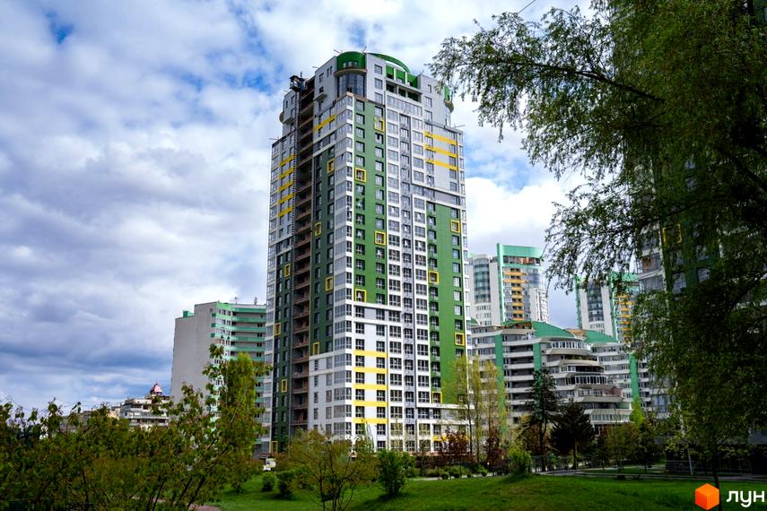 Житловий комплекс Паркове місто: висотні будинки з фасадами зеленого, сірого та жовтого кольорів. Навколо будівель розташовані зелені насадження та газон.