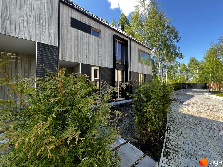 Котеджне містечко КМ Hidden House з дерев'яним фасадом та цегляною основою, з акуратною бруківкою та зеленою територією.
