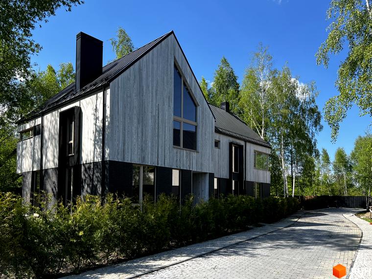 Котеджне містечко КМ Hidden House: двоповерховий будинок з дерев'яним фасадом та чорною цегляною основою, оточений зеленню та вимощеною доріжкою.