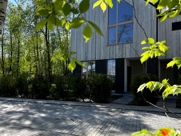 Котеджне містечко КМ Hidden House. Фасад будинку оздоблений дерев'яними панелями, великі вікна. Прибудинкова територія з бруківкою та зеленими насадженнями.