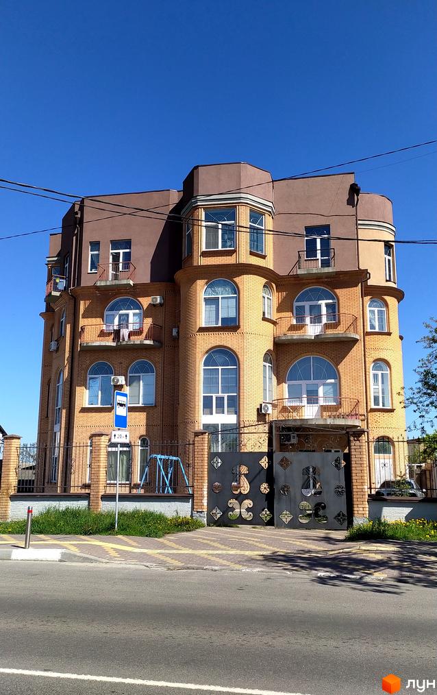 Житловий комплекс Жулянський - цегляна багатоповерхова будівля з арочними вікнами та балконами, огороджена парканом з кованими елементами.