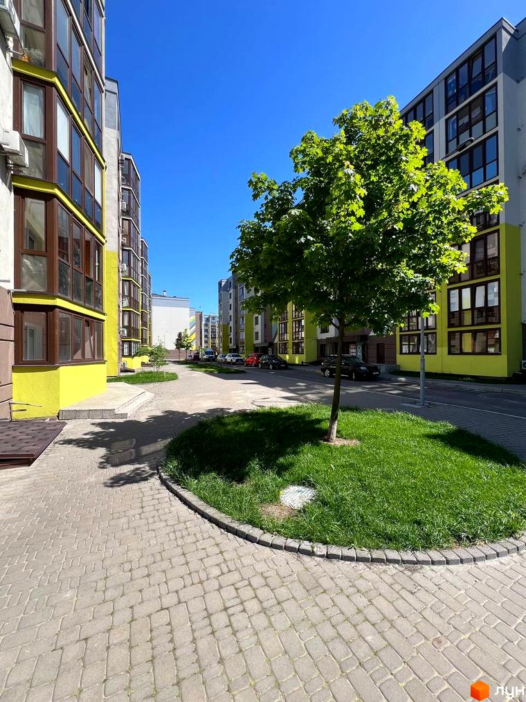 Житловий комплекс Welcome Home на Стеценка. Високі будинки з великими вікнами та жовтими фасадами. На передньому плані бруківка та зелена галявина з деревом.