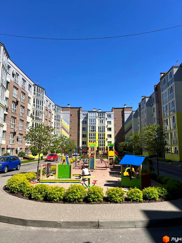 Новобудова ЖК Welcome Home на Стеценка з яскравим фасадом та дитячим майданчиком. Зелена прибудинкова територія з кущами та деревами.